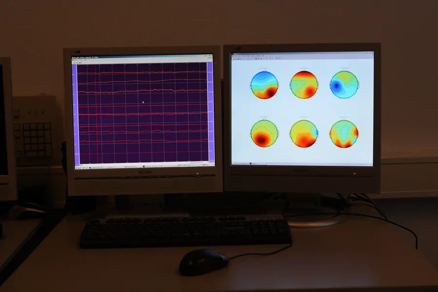 Twee beeldschermen met EEG-signalen en kleurige hersenkaarten